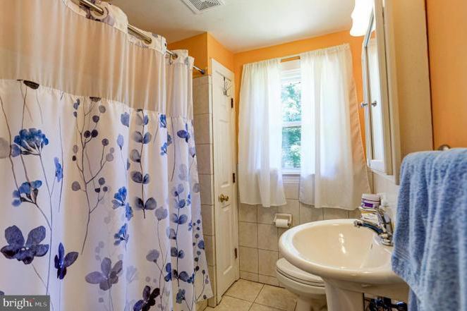 Before: the previous full bathroom with orange walls, a pedestal sink and a shower curtain.
