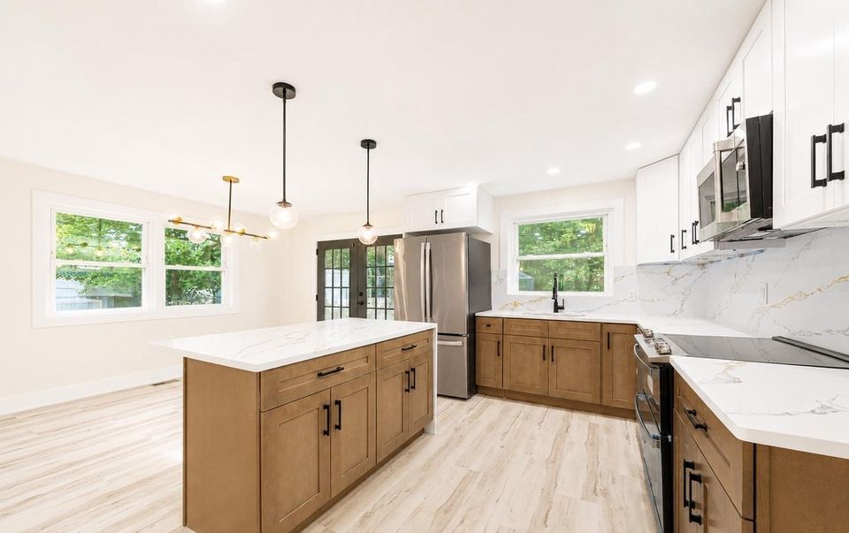 Kitchen with quartz waterfall island, pendant lights, stainless refrigerator and two-tone cabinetry.