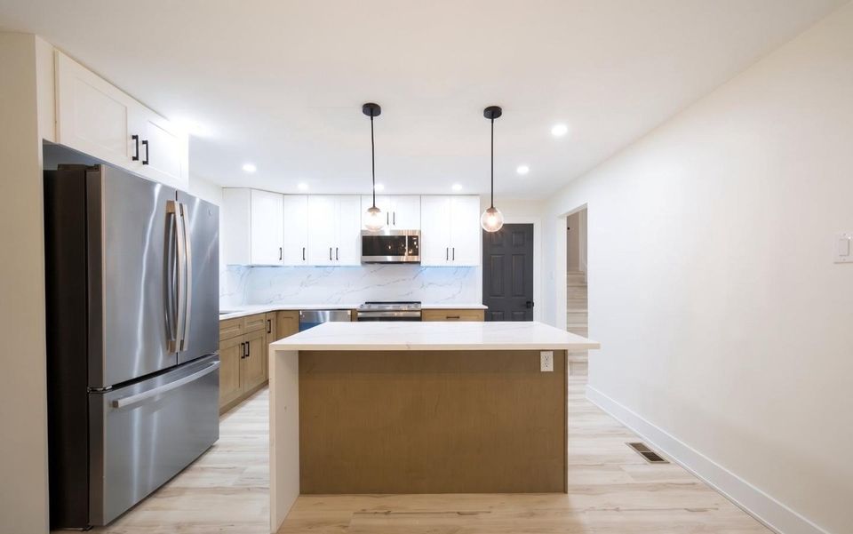Kitchen island with quartz waterfall top seen from the refrigerator side, looking toward the living room.