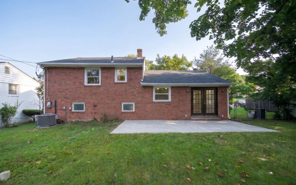 Rear of the home with brick facade, French doors, concrete patio, new air-conditioning condenser and level lawn.