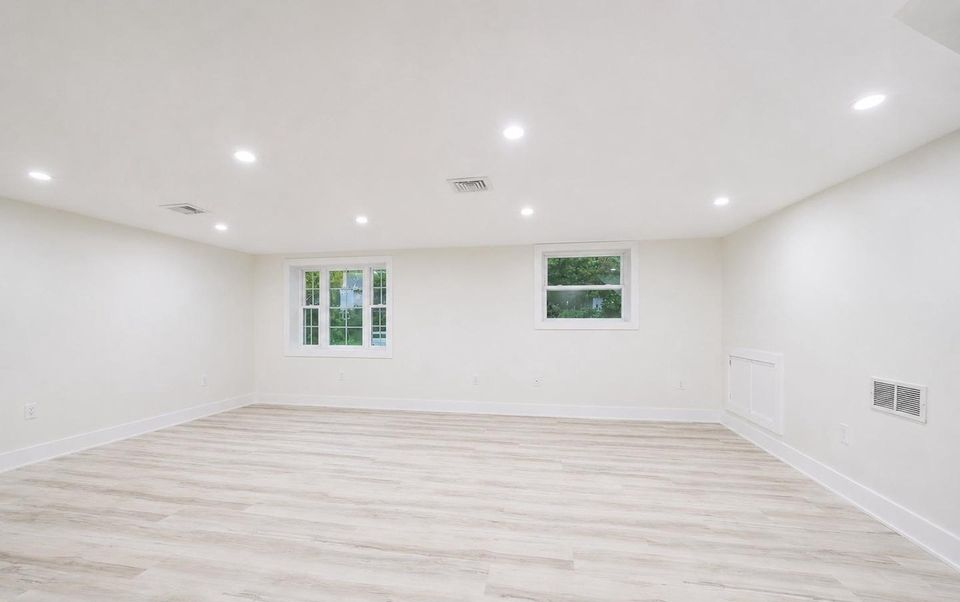 Lower-level recreation room with two windows, recessed lighting and wide-plank flooring.